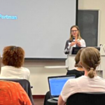 Professor Christine Crawford stands in front of students with a screen behind her